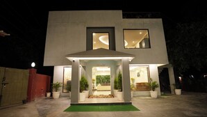 Un edificio moderno de dos pisos con un acceso cubierto, plantas en macetas y un área de recepción visible.