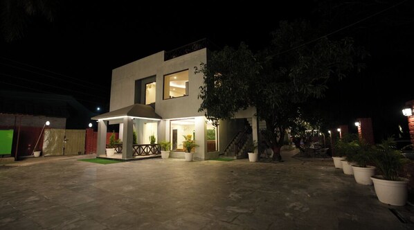 A modern two-story house with a patio area, potted plants, and a staircase leading to the upper floor.