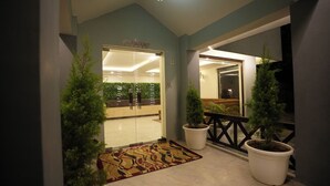Entrada de hotel con mostrador de recepción, plantas en macetas y una alfombra estampada.