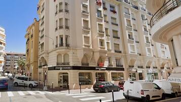 Un hôtel à plusieurs étages, doté de balcons, d’une devanture de magasin et de voitures garées.