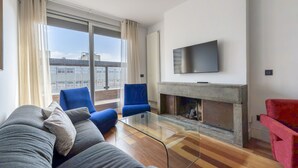 A modern living room with a sofa, two armchairs, a glass coffee table, a flat-screen TV, and a fireplace. - 3 Bedroom Duplex - Spacious, Bright near the Paseo de la Castellana (Madrid)