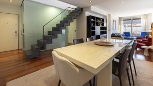 A modern living space with a staircase, a dining area with a long table, and a seating area with chairs and a sofa. - 3 Bedroom Duplex - Spacious, Bright near the Paseo de la Castellana (Madrid)