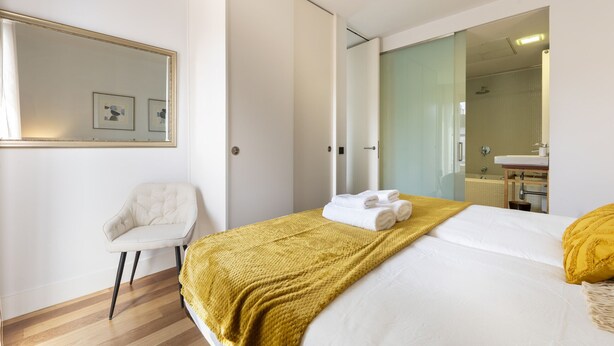 A modern hotel room with a bed, a chair, a mirror, and a bathroom visible through an open door. - 3 Bedroom Duplex - Spacious, Bright near the Paseo de la Castellana (Madrid)