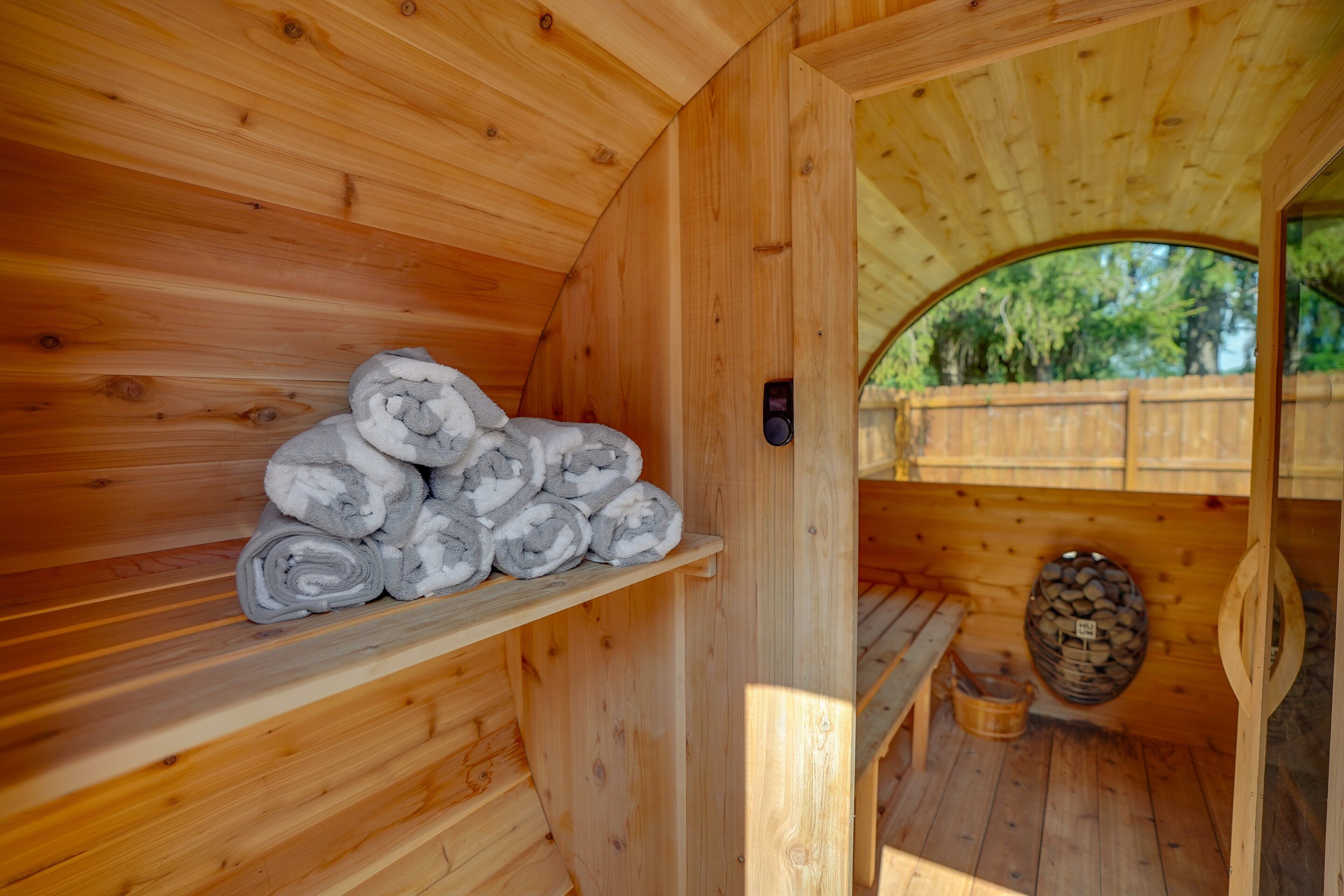 Una sauna de madera con un estante que sostiene toallas enrolladas, un banco y un espacio para almacenar leña.