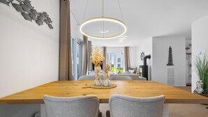 Un comedor moderno con una mesa de madera, dos sillas tapizadas de gris, un florero decorativo y una lámpara colgante.