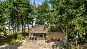 Une cabane rustique avec des fondations en pierre, un toit en tuiles et un espace patio aménagé avec des sièges d’extérieur.