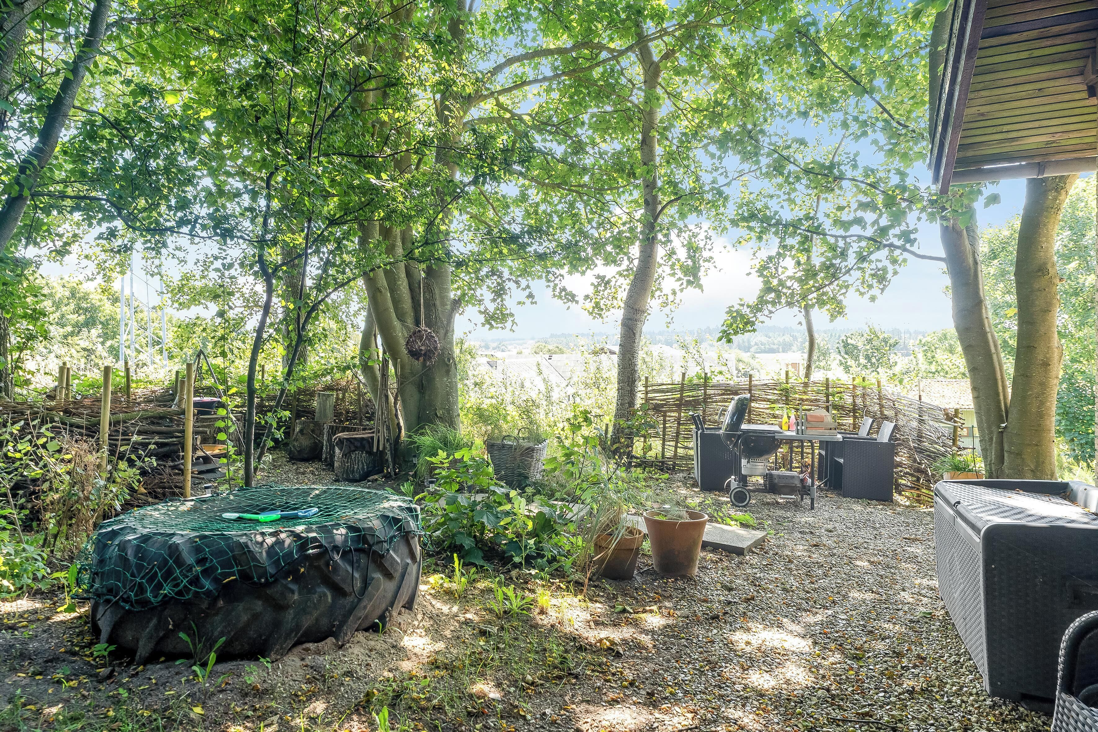 Ein Außenbereich zum Sitzen mit Tisch und Stühlen, umgeben von Bäumen und Blick auf die Landschaft.