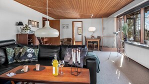 Un salon moderne avec un plafond en bois, un canapé en cuir et un coin repas comprenant une table et des chaises.