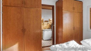 Une chambre à coucher avec des armoires en bois, un lit avec une literie blanche, et une salle de bain visible à travers une porte ouverte.