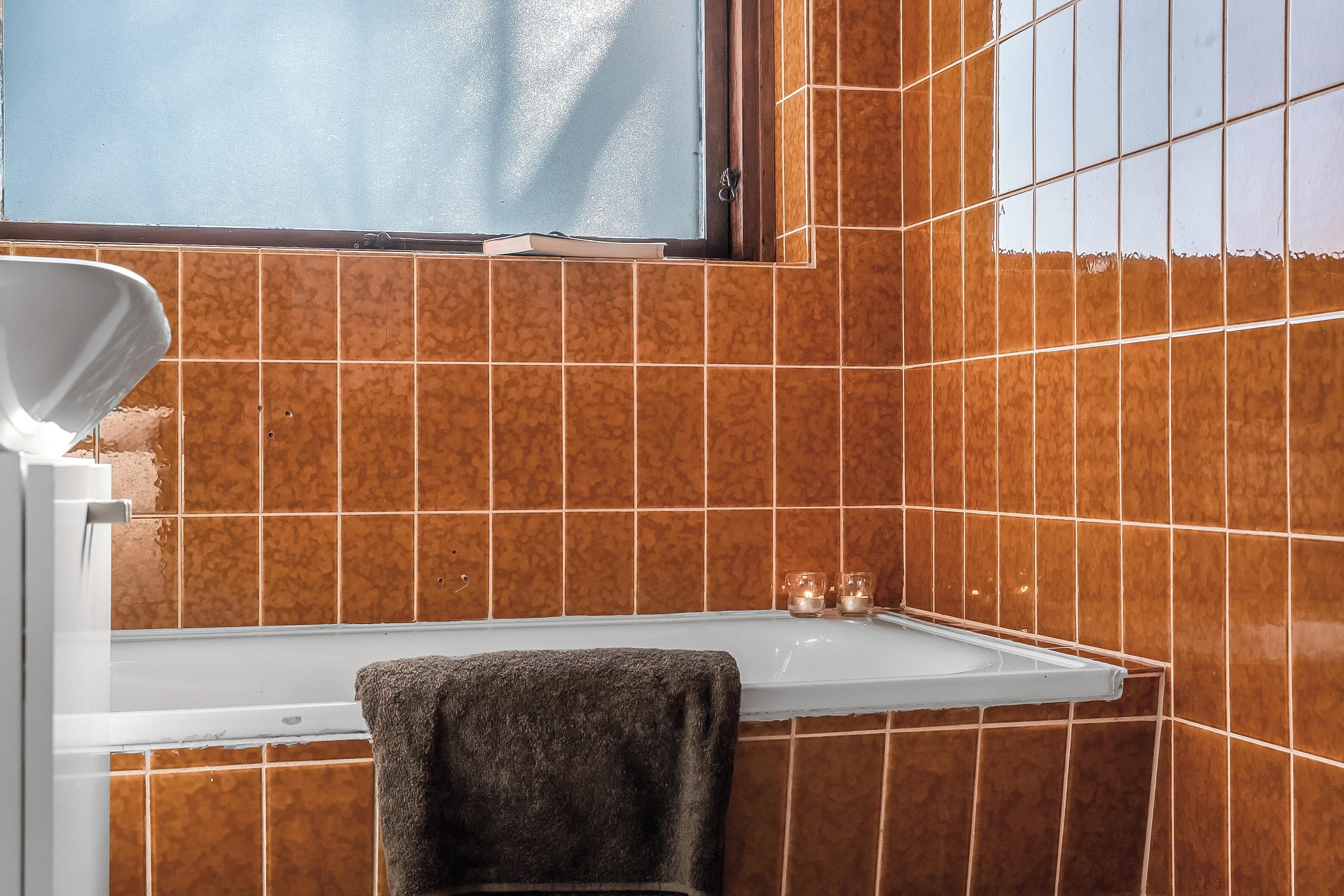 A bathroom with brown tiles, a white bathtub, and a towel hanging on the wall.