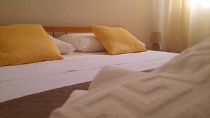 A bed with white bedding and two yellow pillows, a wooden headboard, and a bedside lamp. - Grandfather's House (Balestrate)