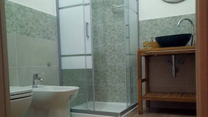 A bathroom with a toilet, bidet, glass shower enclosure, and a wooden vanity with a sink. - Grandfather's House (Balestrate)
