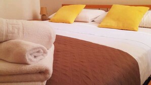 A neatly made bed with a brown bedspread and two yellow pillows, a folded white towel, and a bedside lamp on a wooden nightstand. - Grandfather's House (Balestrate)