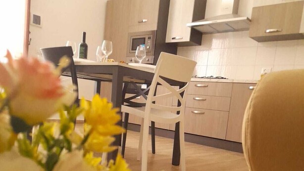 A modern kitchen with wooden cabinets, a dining table with chairs, and a vase of flowers on the table. - Grandfather's House (Balestrate)