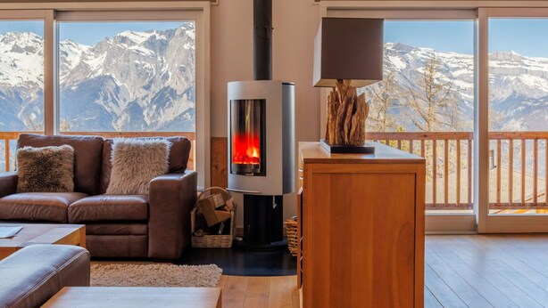 Un salon chaleureux avec une cheminée, un canapé et une vue sur des montagnes enneigées, visible à travers de grandes fenêtres.