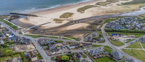 An aerial view of a coastal town with a beach, a bridge, and residential areas.