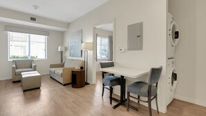 A modern living room with a sofa, a coffee table, and a dining area with chairs. There is a washing machine in the corner. - Simplicity At the Rim 1119 I Spacious 1 Bed 1 Bth (San Antonio)