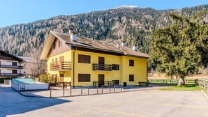 A yellow building with a balcony, a parking area, and a mountain in the background.