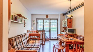 A cozy living room with a sofa, wooden chairs, a dining table, and a television.