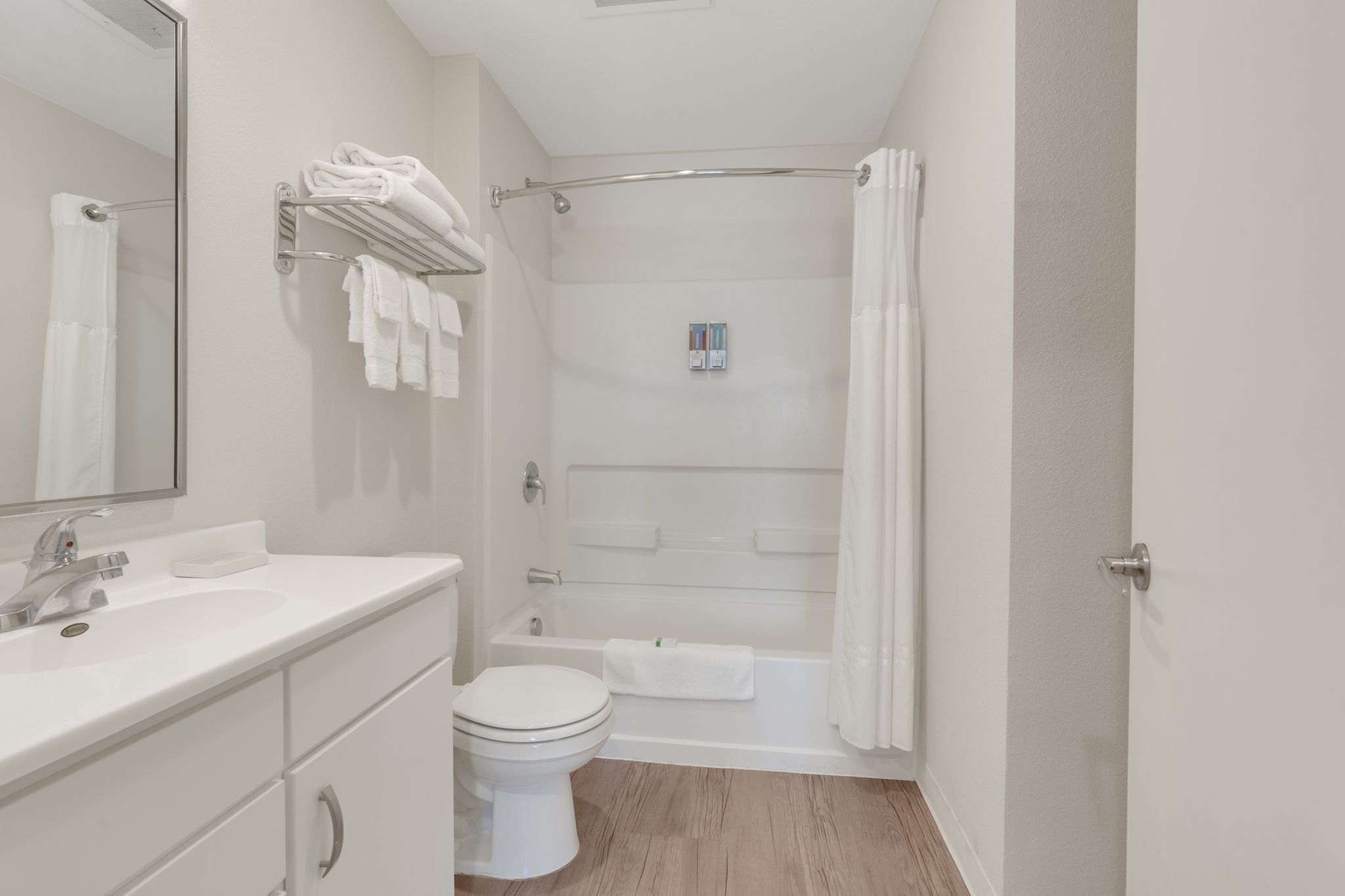 A bathroom with a white sink, toilet, and bathtub. There is a towel rack with folded towels and a shower curtain.