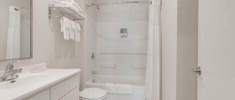 A bathroom with a white sink, toilet, and bathtub. There is a towel rack with folded towels and a shower curtain.