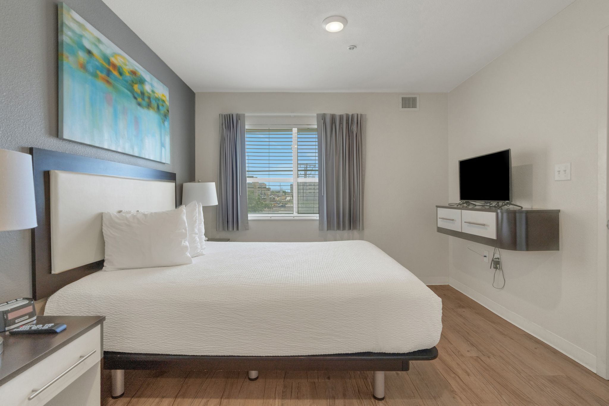Une chambre d’hôtel moderne avec un grand lit, un téléviseur à écran plat, un bureau avec une lampe et un tableau au mur.