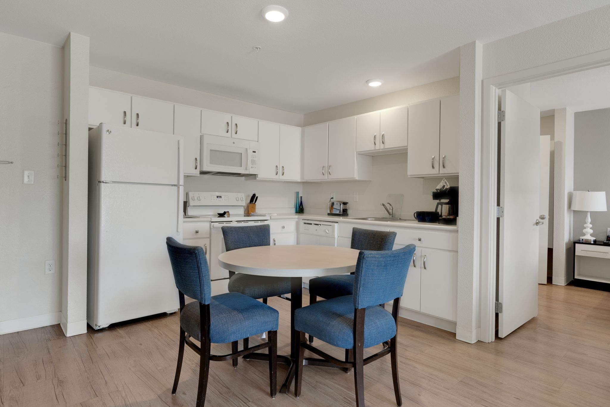 A modern kitchen with white cabinets, a microwave, and a dining table with four chairs.
