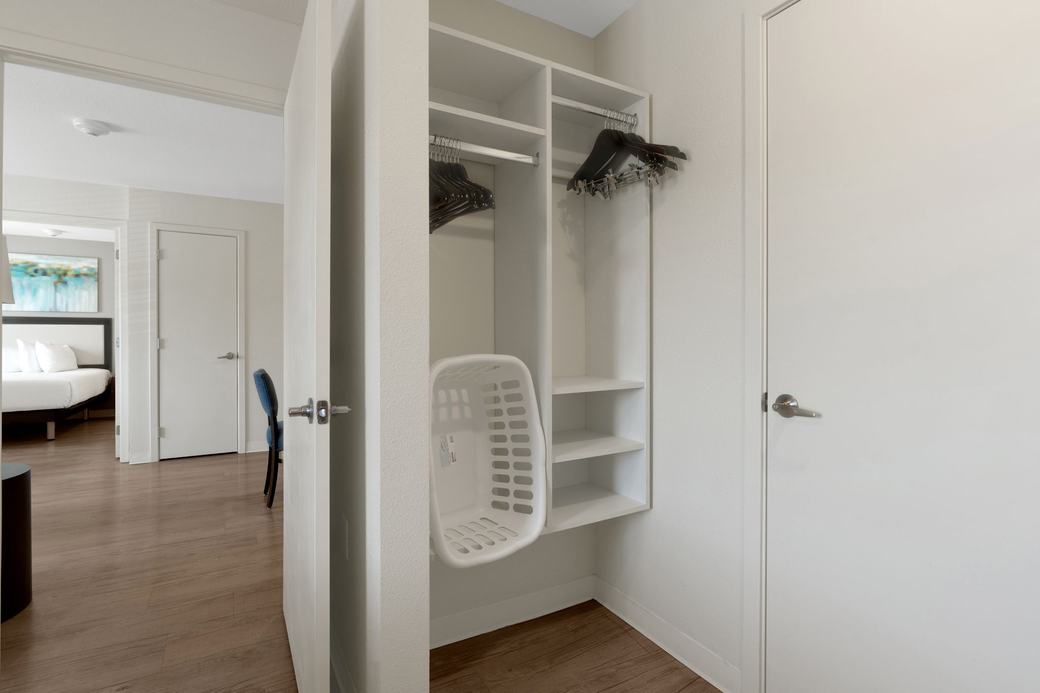 A walk-in closet with hanging space and shelves, a laundry basket, and a door leading to another room.