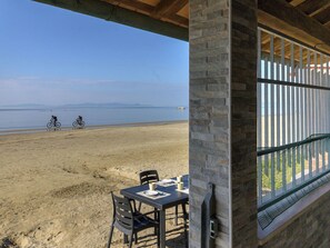 A beach view from a covered patio with a table and chairs, overlooking the beach and a distant shoreline. - Wonderful private villa for 6 guests with A/C, WIFI, balcony and pets allowed (Follonica)