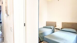 Ett hotellrum med två sängar, ett nattduksbord med en lampa och en dörr som leder ut till en hall.