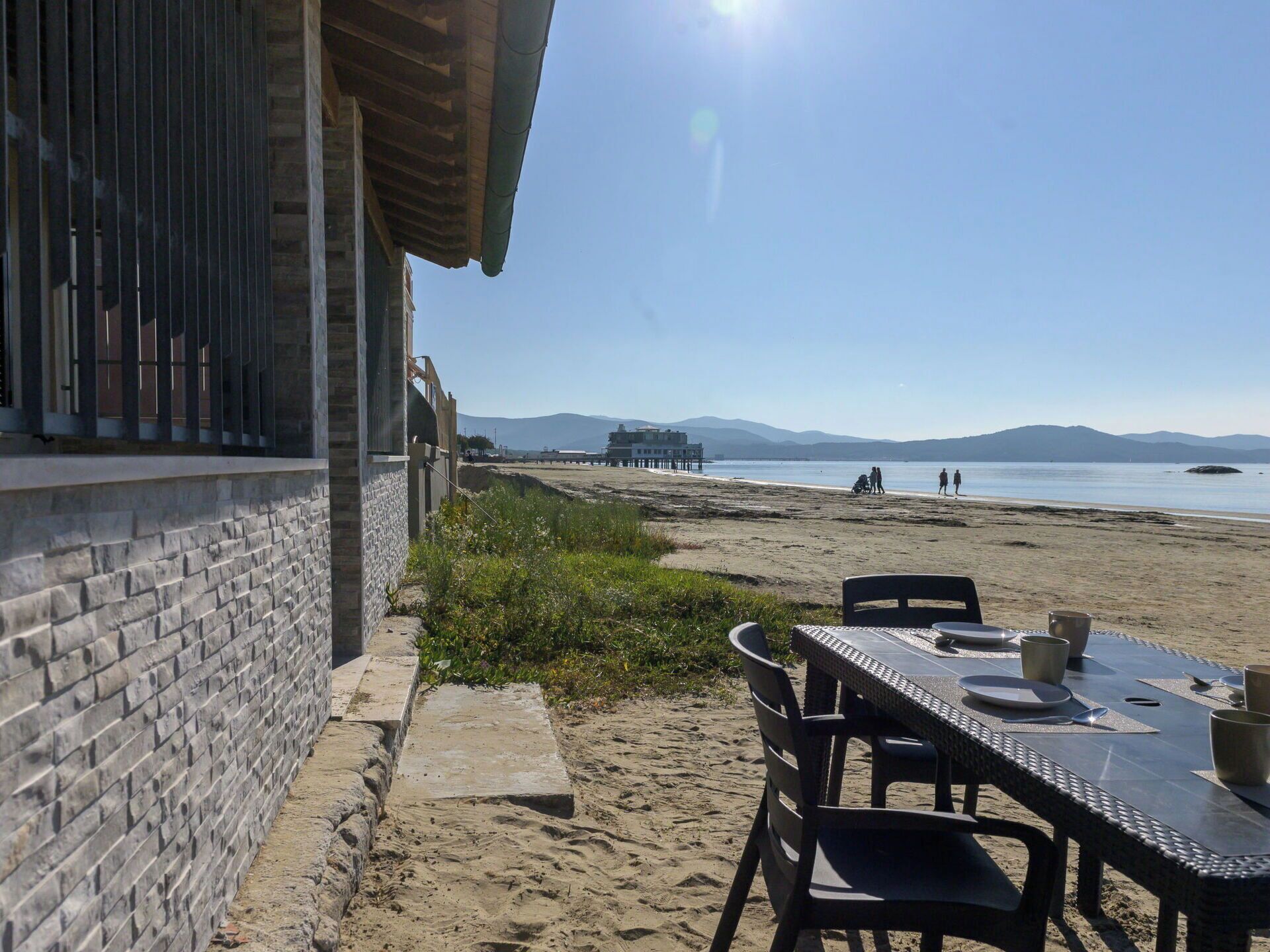 A beachside restaurant with a table set for two, overlooking the sea and a pier in the distance.