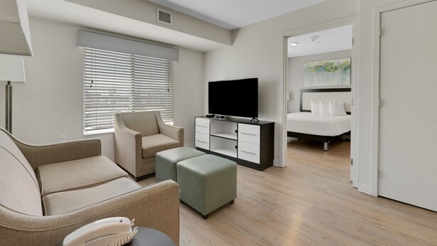 Une chambre d’hôtel moderne équipée d’un canapé, d’un pouf, d’une télévision et d’un lit avec une tête de lit.