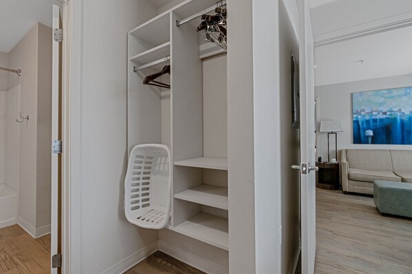 Un closet espacioso con puertas abiertas, una barra para colgar ropa y un cesto de ropa.