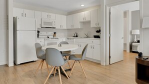 Une cuisine moderne avec des meubles blancs, une table à manger blanche accompagnée de quatre chaises et un plancher en bois.
