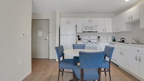 A modern kitchen with white cabinets, a microwave, and a dining area with blue chairs.