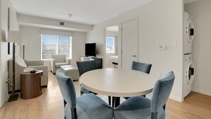 A modern living room with a round table and blue chairs, a sofa, a TV, and a washing machine.