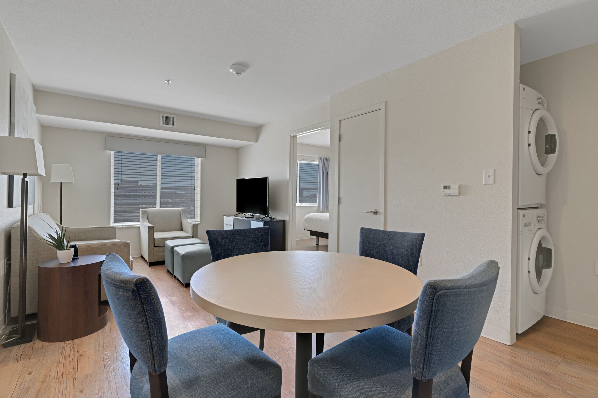 A modern living room with a round table, blue chairs, a sofa, a TV, and a washing machine.
