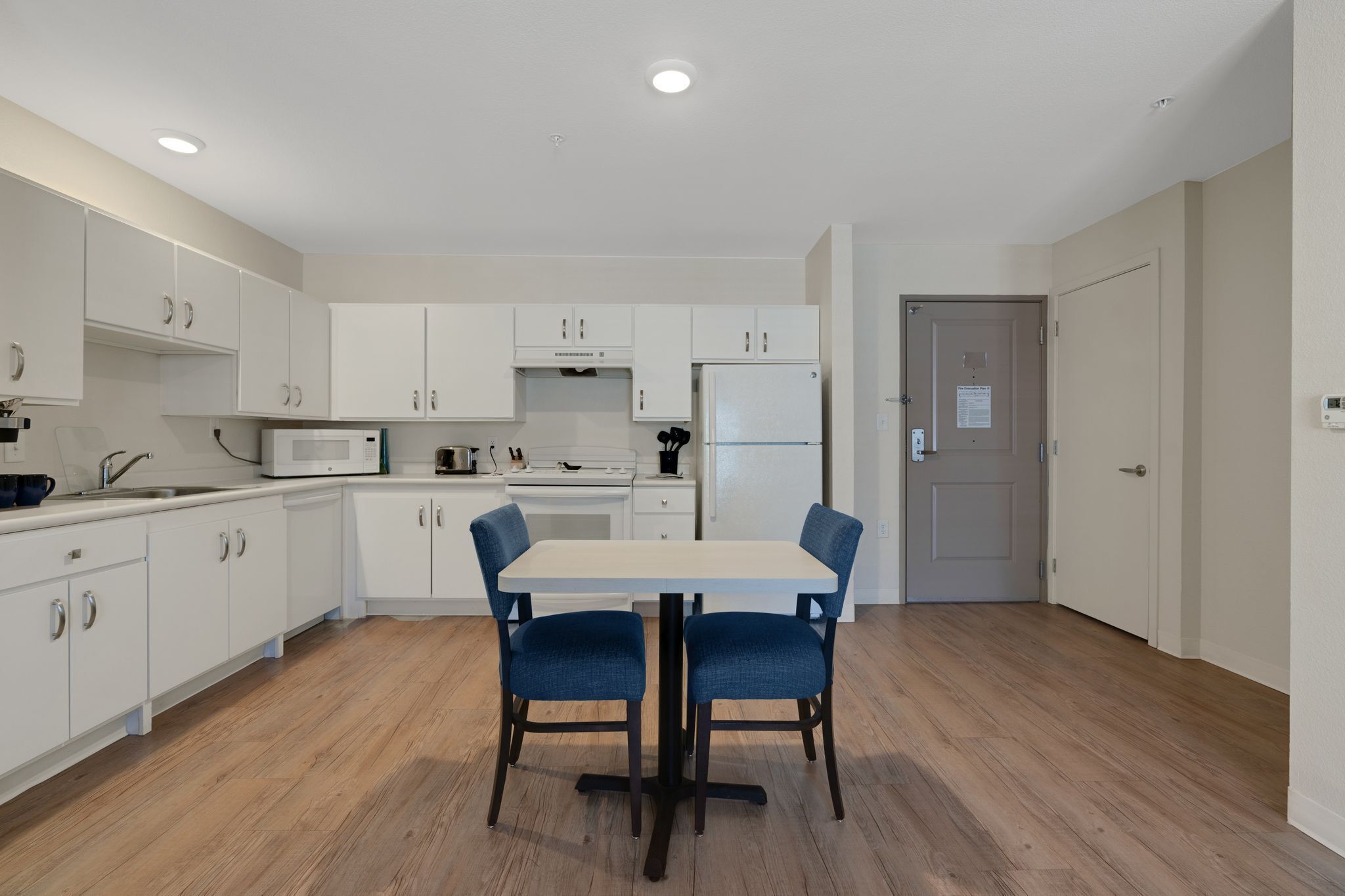 A modern kitchen with white cabinets, a microwave, a stove, and a refrigerator. There is a dining table with two chairs.