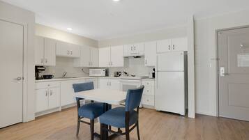 A modern kitchen with white cabinets, a dining table with two chairs, and a refrigerator.