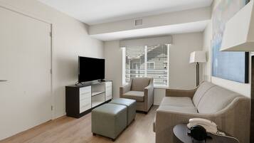 A modern living room with a flat-screen TV, a sofa, a coffee table, and a window with blinds.