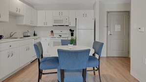 A modern kitchen with white cabinets, a microwave, a refrigerator, and a dining table with blue chairs.