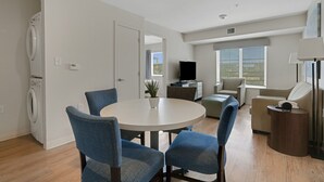 A modern living room with a round table, blue chairs, a sofa, a TV, and a washing machine.
