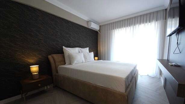 A modern hotel room with a large bed, a dark textured wall, a bedside table with a lamp, and a large window with curtains. - Ganzo Boutique Hotel (Bucharest)