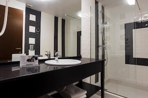 Un baño moderno con encimera negra, lavabo blanco y cabina de ducha con mampara de cristal.