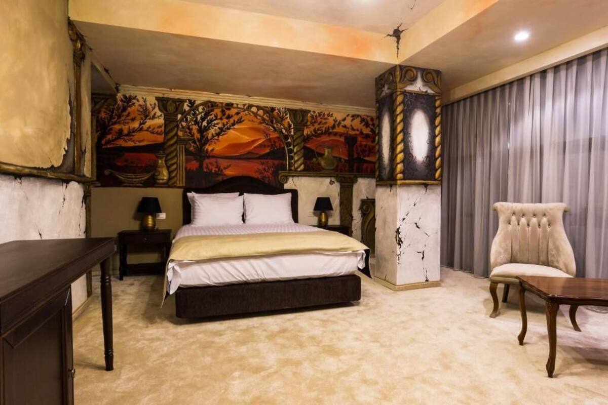 A bedroom with a large bed, a chair, a table, and a decorative wall mural.