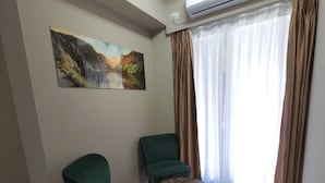 A living room with two green chairs, a round coffee table, a painting on the wall, and an air conditioning unit above a window with brown curtains. - Ganzo Boutique Hotel (Bucharest)