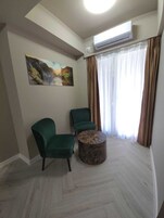 A living room with two green chairs, a round coffee table, a painting on the wall, and an air conditioning unit above a window with brown curtains.