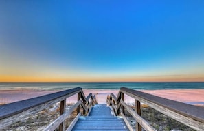 Une promenade en bois menant à une plage, avec un ciel dégagé.