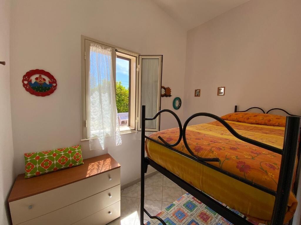 A bedroom with a bunk bed, a dresser, a window with curtains, and a view of greenery outside.