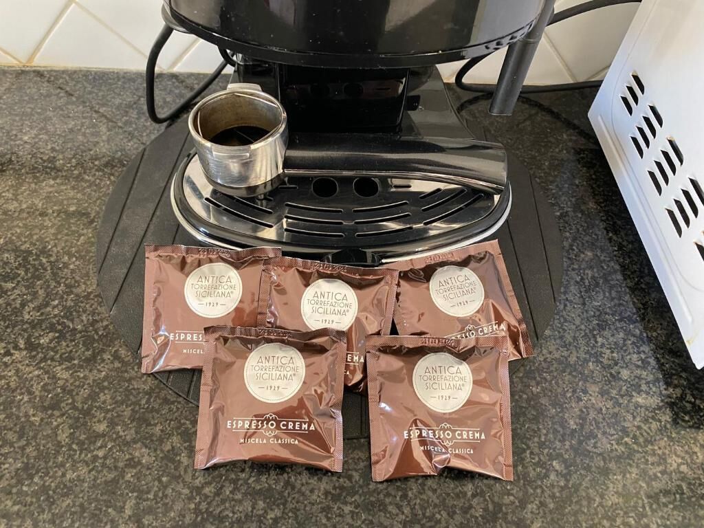 A coffee machine and four packets of coffee labeled "ANTICA TORREFAZIONE SICILIANA" on a kitchen counter.